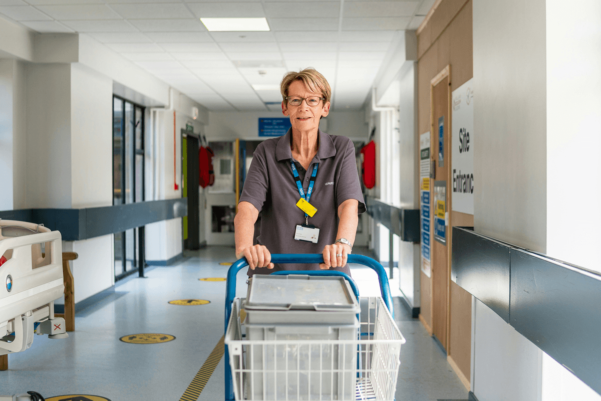 Lady working in NHS pushing trolley down hospital hall
